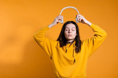 Müzik severler müzikten hoşlanır. Beyaz kablosuz kulaklıklı sarı kapüşonlu genç bir kadın.,