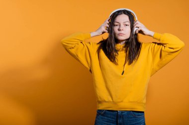 Müzik severler müzikten hoşlanır. Beyaz kablosuz kulaklıklı sarı kapüşonlu genç bir kadın.,
