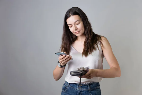 Ελέγξτε τον τραπεζικό σας λογαριασμό στην εφαρμογή στο smartphone σας. Μια νεαρή γυναίκα με πορτοφόλι και τηλέφωνο. — Φωτογραφία Αρχείου