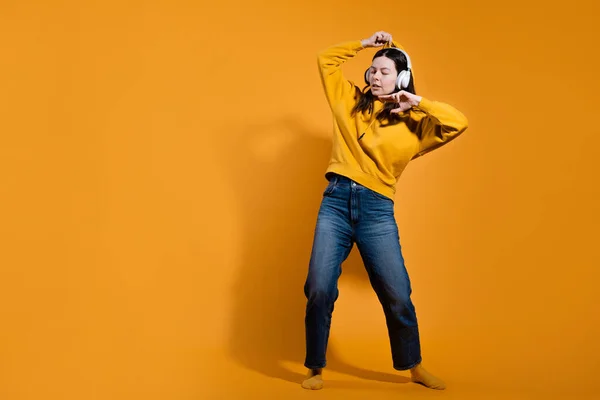 Glücklich tanzender Musikliebhaber. Eine junge Frau in einem gelben Kapuzenpullover mit weißen drahtlosen Kopfhörern, — Stockfoto