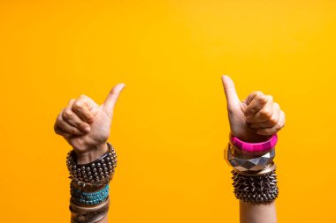 El hareketleriyle. Baş parmaklar yukarı, onay gibi. Bir sürü bileziği olan iki kadın eli, gençlerin eğlence tarzı..