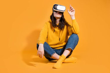 Sarı arka planda sanal gerçeklik cihazı olan genç bir kadın..