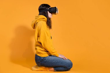 Sarı arka planda sanal gerçeklik cihazı olan genç bir kadın..