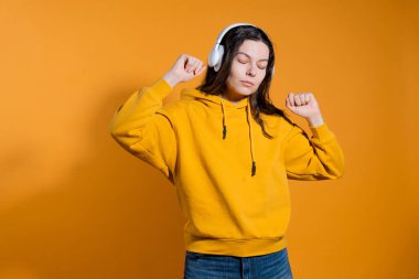 Mutlu dans müziği severler. Beyaz kablosuz kulaklıklı sarı kapüşonlu genç bir kadın.,