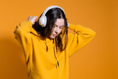 Müzik severler müzikten hoşlanır. Beyaz kablosuz kulaklıklı sarı kapüşonlu genç bir kadın.,
