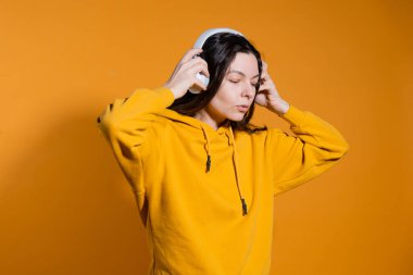 Müzik severler müzikten hoşlanır. Beyaz kablosuz kulaklıklı sarı kapüşonlu genç bir kadın.,