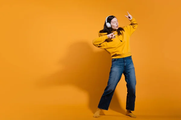 Glücklich tanzender Musikliebhaber. Eine junge Frau in einem gelben Kapuzenpullover mit weißen drahtlosen Kopfhörern, — Stockfoto