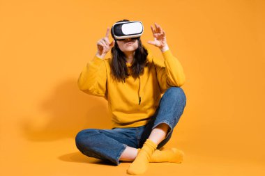Sarı arka planda sanal gerçeklik cihazı olan genç bir kadın..