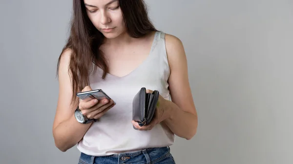 Check your bank account in the app on your smartphone. A young woman with a wallet and phone — Stock Photo, Image