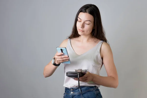 Ελέγξτε τον τραπεζικό σας λογαριασμό στην εφαρμογή στο smartphone σας. Μια νεαρή γυναίκα με πορτοφόλι και τηλέφωνο. — Φωτογραφία Αρχείου