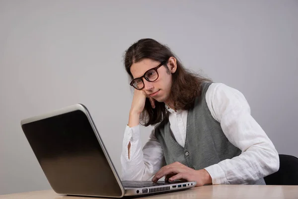 Estudante entediado está sentado em um laptop. O tipo é um jogador cromo, usa um portátil. Curso desinteressante — Fotografia de Stock