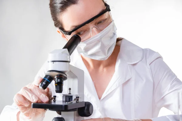 lab technician looks into the eyepiece of a microscope, a young female doctor