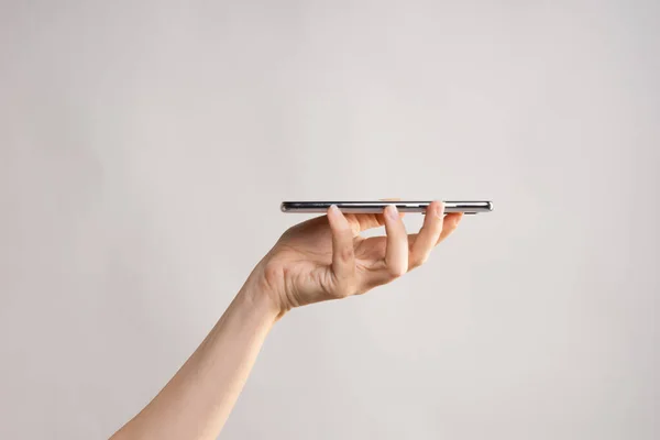 Slim modern smartphone, use the Internet or apps. A womans hand holds the phone horizontally.