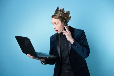 Kafasında taç olan şok olmuş bir işadamı dizüstü bilgisayar ve telefon kullanıyor..