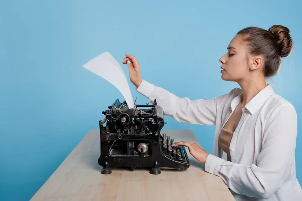 Jonge vrouw auteur bij een typemachine, schrijft een tekst. Een schrijver aan tafel met een vintage typemachine — Stockfoto
