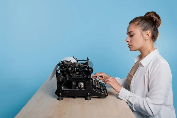 Jonge vrouw auteur bij een typemachine, schrijft een tekst. Een schrijver aan tafel met een vintage typemachine — Stockfoto