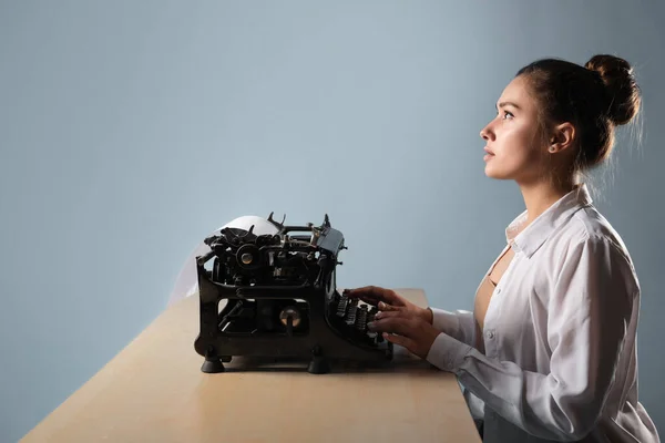 Joven escritora en una máquina de escribir, escribe un texto. Un escritor en una mesa con una máquina de escribir vintage — Foto de Stock