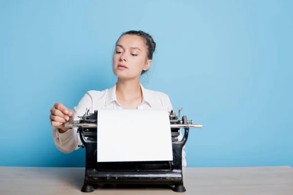 Joven escritora en una máquina de escribir, escribe un texto. Un escritor en una mesa con una máquina de escribir vintage — Foto de Stock