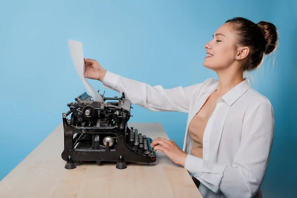 Jonge vrouwelijke schrijver op een typemachine kijkt naar een vel papier met wow emotie, — Stockfoto