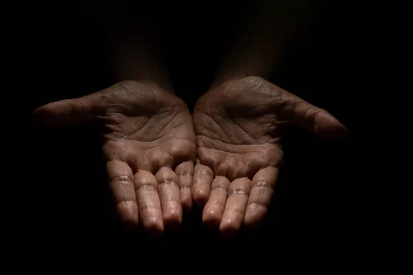 Begging, empty palms, outstretched hands. Concept of social disadvantage, black background.