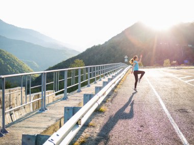 Sabahleyin dağlarda ısınırız. Genç bayan atlıyor ve egzersiz yapıyor.,