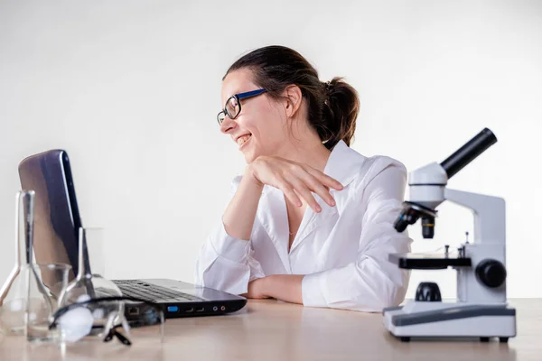 Uma jovem mulher, um assistente de laboratório ou um pesquisador ri enquanto olha para um laptop. — Fotografia de Stock