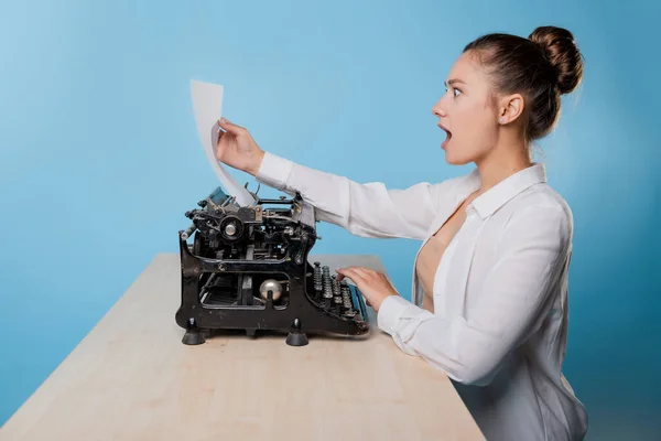Joven escritora en una máquina de escribir mira una hoja de papel con emoción wow, — Foto de Stock