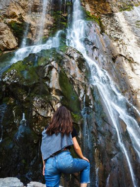 Güzel ve yüksek şelale. Genç bir kadın dağlarda yürüyüş yapıyor..
