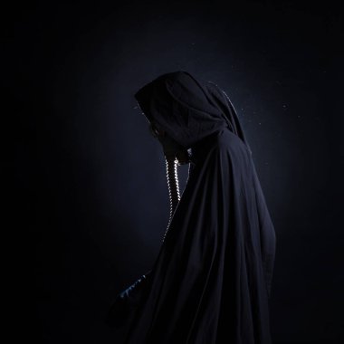 Siyah elbiseli kasvetli bir adam, başında siyah bir başlık, yüzünü koruyan bir gaz maskesi..