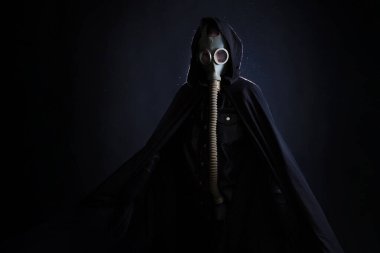 Siyah elbiseli kasvetli bir adam, başında siyah bir başlık, yüzünü koruyan bir gaz maskesi..