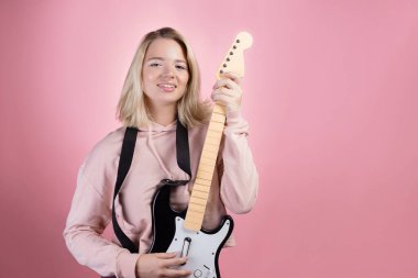Genç ve çekici bir sarışın gülüyor ve oyuncak gitar çalıyor. Eğlence ve hobi..