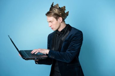 Kafasında taç olan bir iş adamı dizüstü bilgisayar ve telefon kullanıyor..