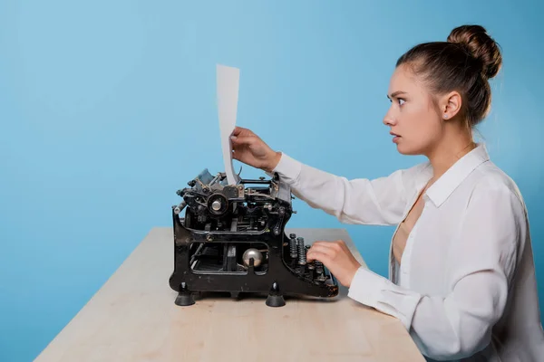 Jonge vrouw schrijver op een typemachine kijkt naar een stuk papier met verrassing, — Stockfoto