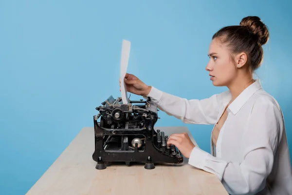 Jonge vrouw schrijver op een typemachine kijkt naar een stuk papier met verrassing, — Stockfoto