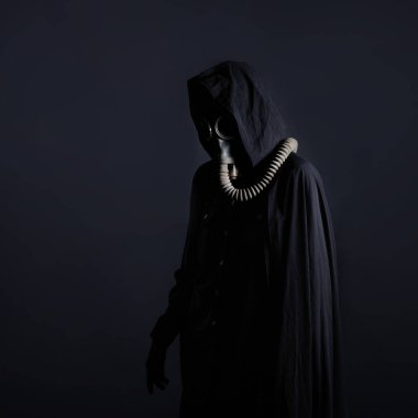 Siyah elbiseli kasvetli bir adam, başında siyah bir başlık, yüzünü koruyan bir gaz maskesi..