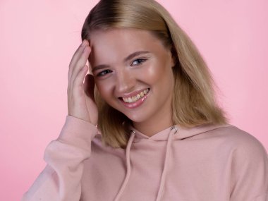 Pembe kapüşonlu genç sarışın mutlu bir şekilde gülümsüyor..