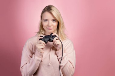 Çekici sarışın oyuncu. Pembe kapüşonlu gülümseyen genç bir kadın kumanda kolu tutuyor.