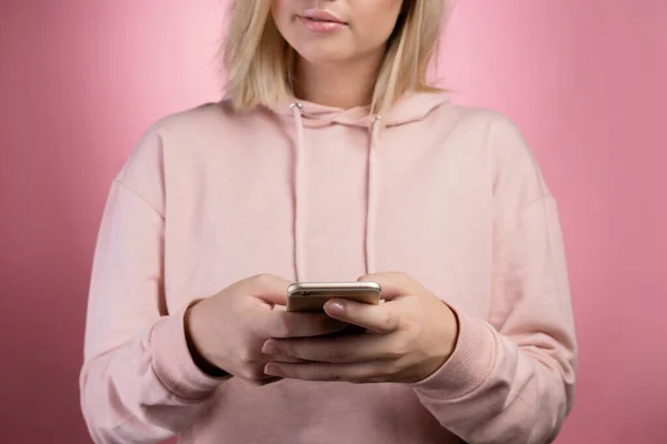 Navegação na Internet, aplicações móveis. Uma jovem atraente em um capuz rosa usa um smartphone. — Fotografia de Stock