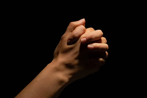 Pregando mani incrociate su uno sfondo nero. Luce dall'alto. Mani giunte in preghiera. — Foto Stock