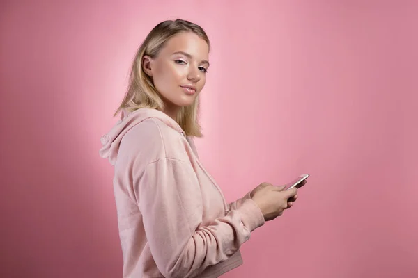 Internet browsing , mobile applications . An attractive young woman in a pink hoodie uses a smartphone.