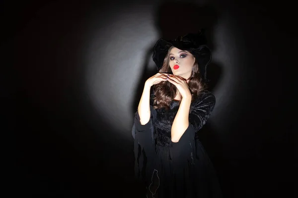 Strega alla festa di Halloween, una giovane bella donna bruna in un classico costume da strega con un cappello a punta — Foto Stock