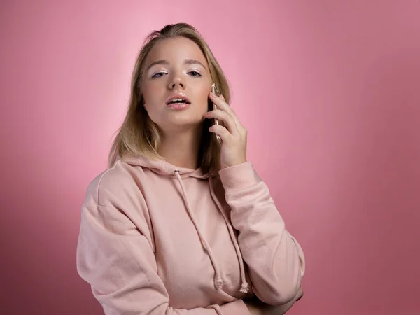 Una giovane donna sta parlando al telefono. Una giovane donna attraente con una felpa rosa — Foto Stock