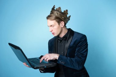 Kafasında taç olan bir iş adamı dizüstü bilgisayar ve telefon kullanıyor..