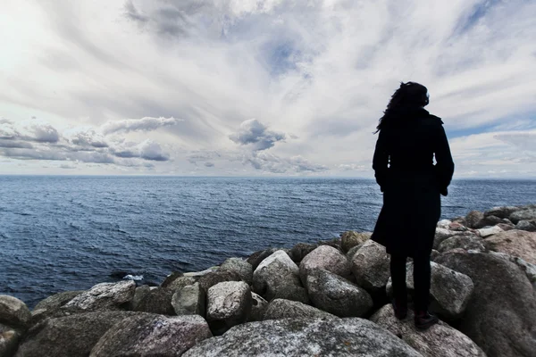 Frau steht auf den Felsen und beobachtet den Sonnenuntergang am Meer, dramatische Aussicht, Frau am Rand, Frauensilhouette ungewöhnlich, Außenseiter-Konzept — Stockfoto