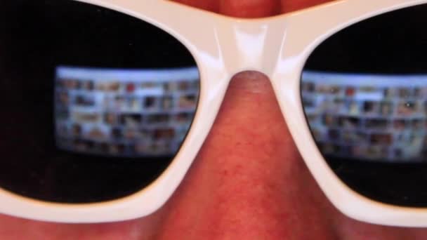 Mannen i glas surfa internet på bärbara datorn på natten, man bläddrar bilder på skärmen med reflektion på solglasögon — Stockvideo