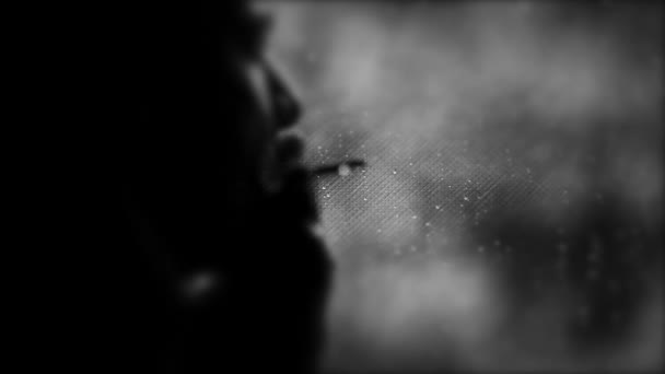 Silhueta de um homem parado junto a uma janela e fumando, olhando pela janela em dia chuvoso, chuva cai na janela — Vídeo de Stock