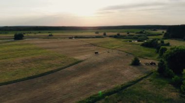 Bir çiftçi traktörünü tarladan geçirip samanlarını toplar ve balyaya çevirir.