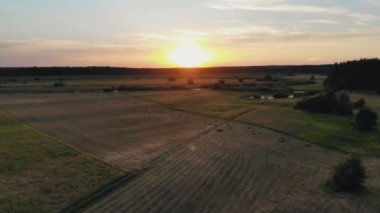 Bir çiftçi traktörünü tarladan geçirip samanlarını toplar ve balyaya çevirir.