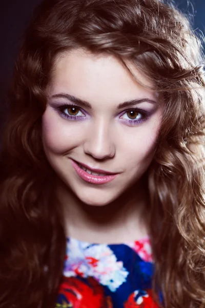 Portrait d'une belle jeune fille avec un sourire doux avec des dents dans une robe bleue avec des fleurs rouges avec de longs cheveux naturels et le maquillage — Photo