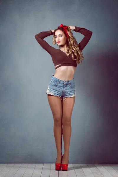 Beautiful young sexy blonde slim figure with a red armband with red lips in denim shorts in red high heels with long legs Pin Up — Stock Photo, Image